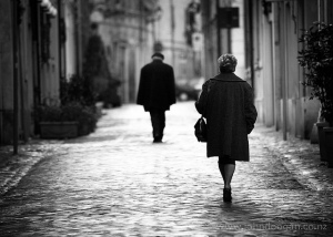 A man and a woman walk away from the camera down a long cobbled street. Senigalia, Italy.